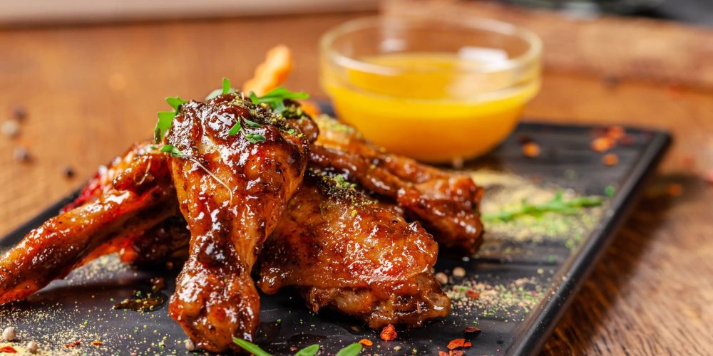 The concept of Indian cuisine. Baked chicken wings and legs in honey mustard sauce. Serving dishes in the restaurant on a black plate. Indian spices on a wooden table. background image.